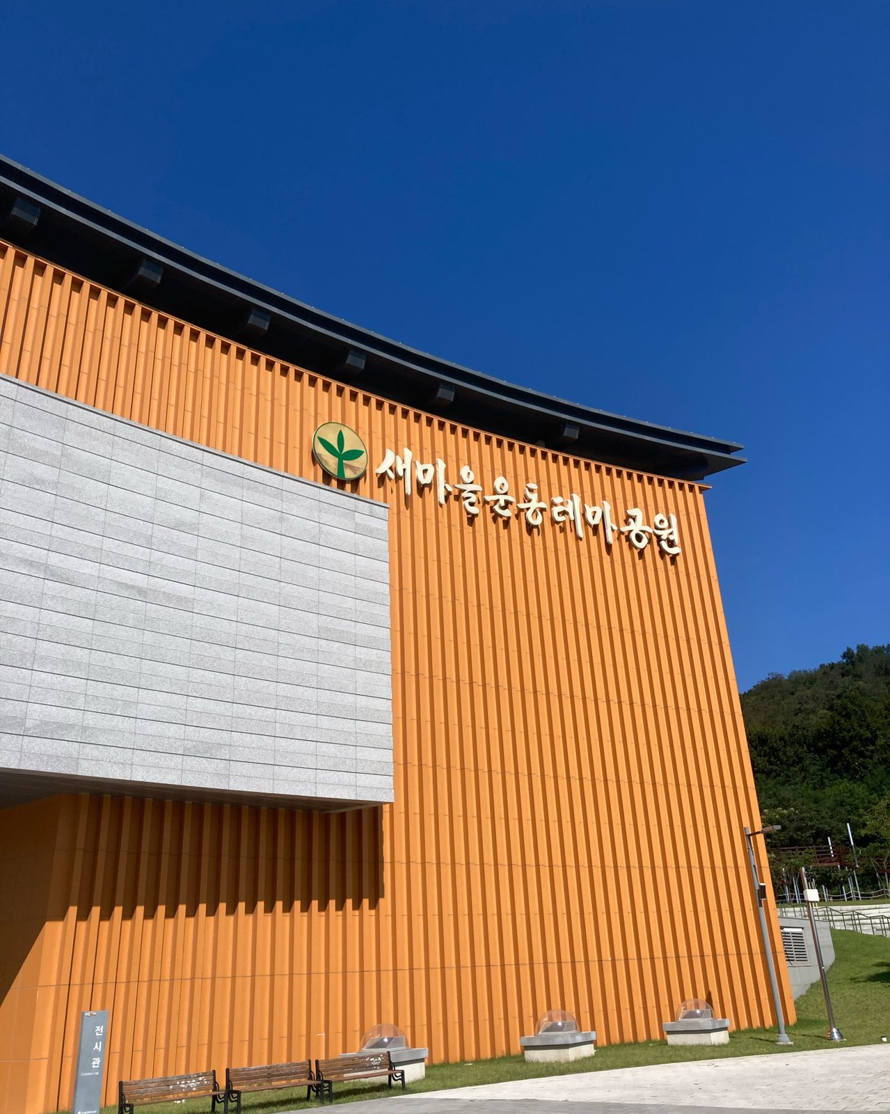 «새마을운동테마공원» 간판이 있는 주황색 세로 외벽과 파란 하늘